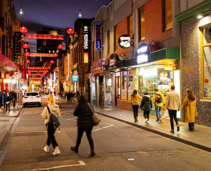 Multiple people walk down the street in Chinatown, Melbourne, at night time.